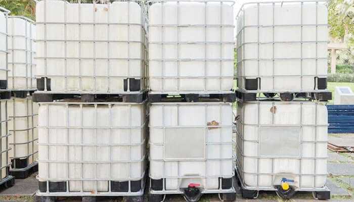 Large industrial used ibc totes containers stacked vertically with a metal cage for transporting or storing bulk liquids.