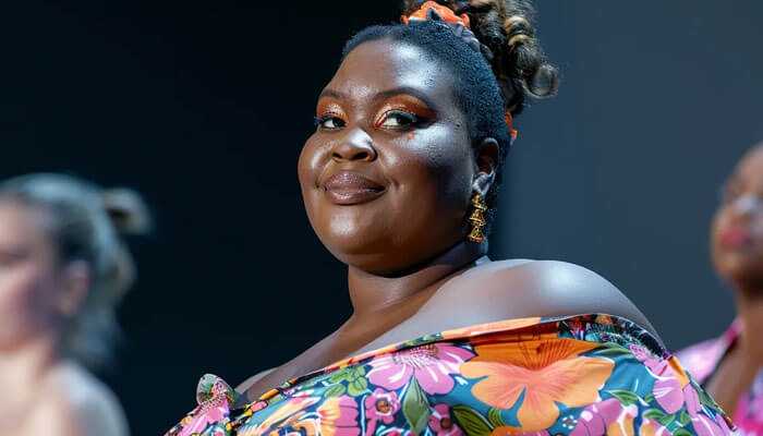 Plus-size model strutting in bright floral off-the-shoulder dress down the runway with confidence.