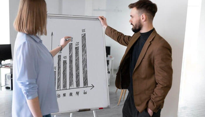 Professionals discussing a whiteboard bar chart to represent analytics driven with the help of small business it services.