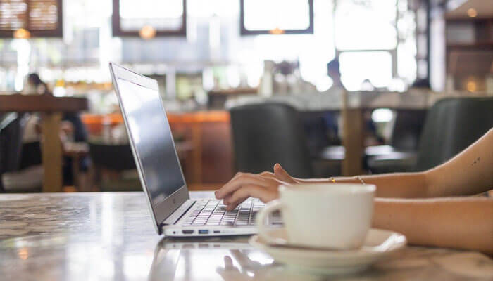 Working on the laptop for remote work in a cozy cafe setting-a cup of coffee on the table-represents the digital nomad lifestyle.