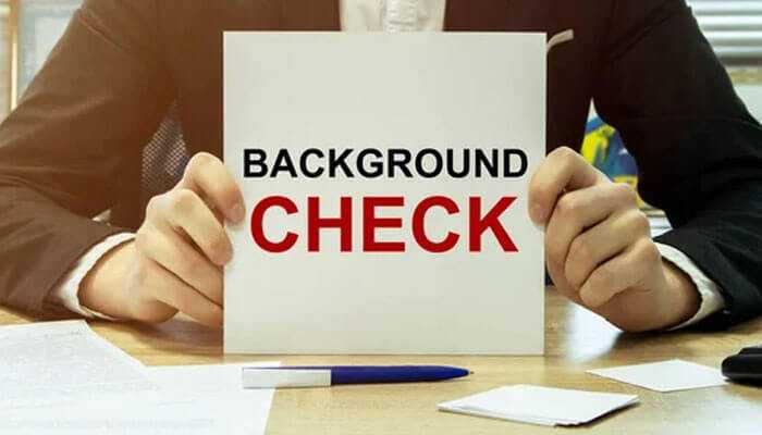 A professional holding a placard showing employee background checks, with documents and a pen on the desk.