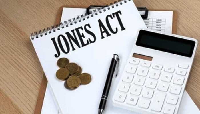 A notepad with jones act text, coins, a pen, and a calculator on the desk, symbolizing financial and legal matters.