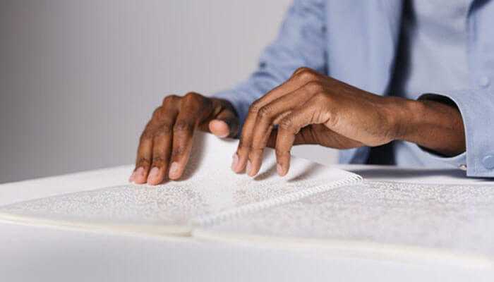 Hands reading a braille book, representing accessibility features in appointment scheduling software for visually impaired individuals.