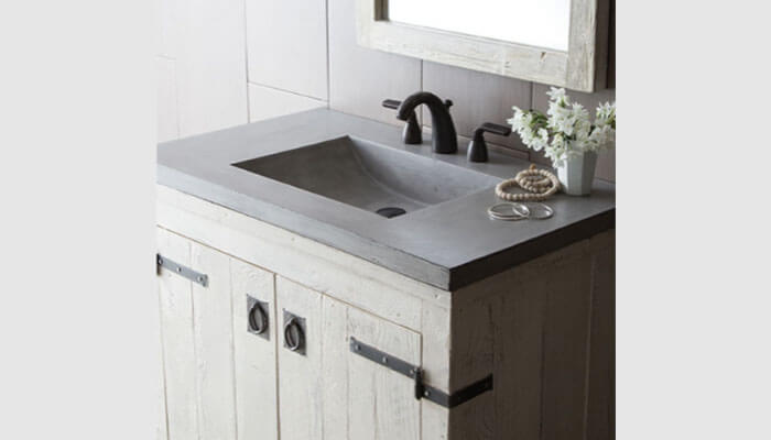 A rustic bathroom sink with a concrete countertop, black faucet, wooden vanity, and matching framed mirror, enhanced by simple decor—a perfect choice when buying a bathroom sink.