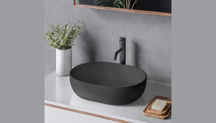 Buying a bathroom sink: a simple black vessel sink with a minimalist faucet on a white countertop, accompanied by a plant and soap tray to give it that modern feel.