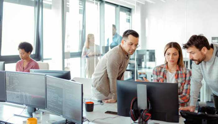 A team of professionals working together in a modern office, reviewing code on multiple screens. The image represents collaboration and innovation in leading custom software development companies.