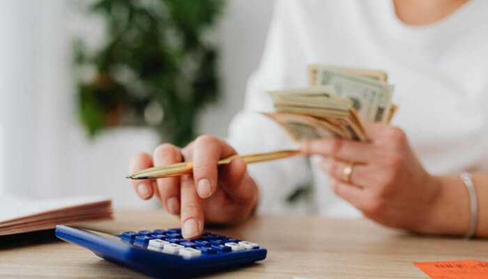 A woman holding cash and using a calculator to manage personal finances—analyzing the real pros and cons of debts and exploring debt consolidation options.