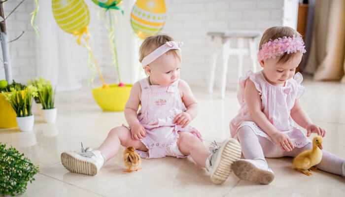 Adorable baby girls in pink patpat clothes playing indoors with ducklings.