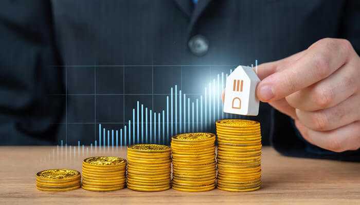 Stacks of gold coins increasing in height with a hand placing a house model on top, representing financial growth and investment during the stages of wealth.