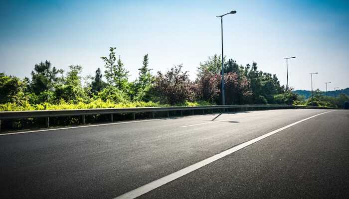 Clear asphalt road with greenery along the sides, highlighted by street lights, offering a scenic, open roadway view.