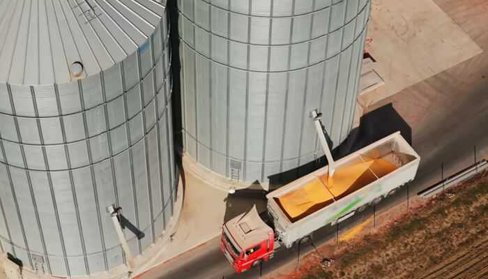 A red truck being loaded with grain from large metal silos at an agricultural facility, showcasing efficient grain management operations.