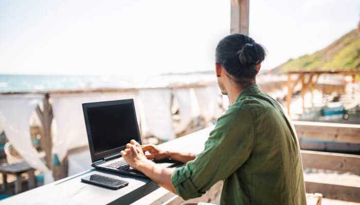 Why more people are chasing the sun 1 | tycoonstory media Man embracing work life balance in sunny location, using a laptop at a beachside workspace with ocean in the background.