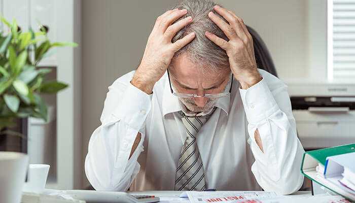 Senior businessman with head in hands at desk, illustrating the consequences of misconduct and director disqualification in UK.