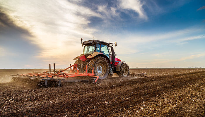 Tractor pulling soil tillage tractor implements to prepare farmland under a bright sky.