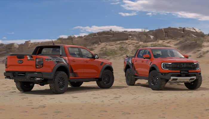 Two ford ranger raptors in bright orange displayed on rocky terrain, highlighting the truck’s aggressive styling and adventure-ready stance.