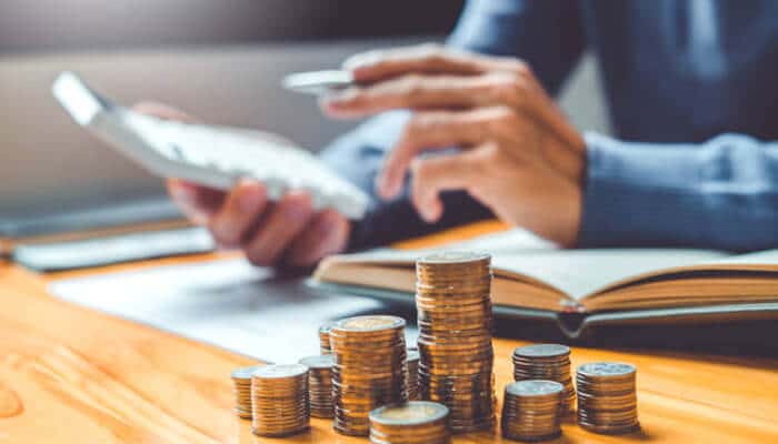 Person using a calculator with stacked coins on a desk, representing financial analysis and adapting your budget to achieve savings and long-term stability.