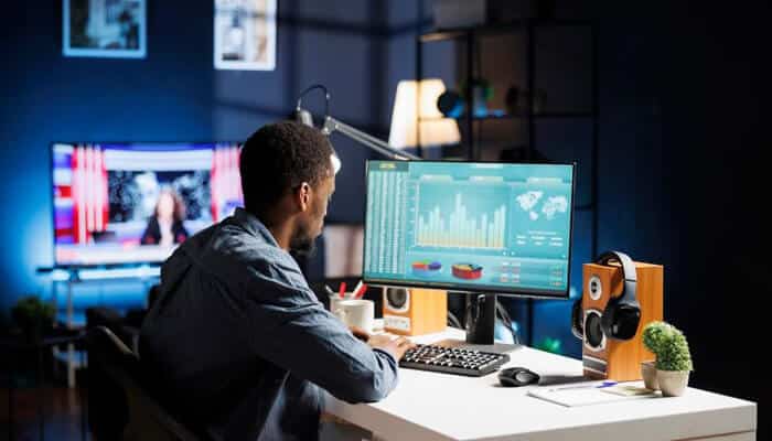 A content creator working at a desk with dual monitors, one showing analytics and charts, representing different thumbnail styles and data-driven design choices for digital and video content.