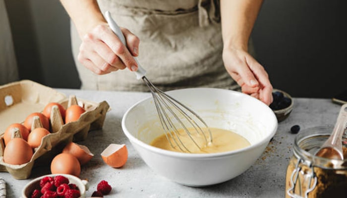 A person whisking batter in a bowl, surrounded by fresh eggs and berries. This image showcases how women can make money fast as a woman by offering home-based baking services or starting a small food business.
