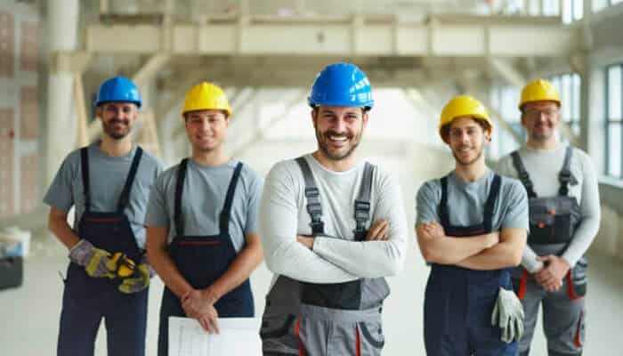 Group of smiling construction workers wearing safety helmets and work overalls, standing confidently inside an industrial building, representing teamwork and professionalism in gold coast’s labour hire industry.