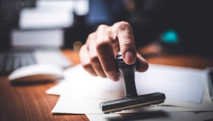 A hand stamping an'APPROVED' mark on a document, symbolizing the approval process for a vending machine business proposal.