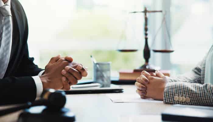 Legal risks for manufacturers and distributors | tycoonstory media A close-up of a lawyer and client meeting to discuss legal risks, with the scales of justice in the background. The conversation focuses on defective medical devices and potential liabilities for manufacturers and distributors.
