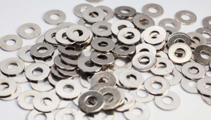 Pile of small metal washers scattered on a white surface, shiny and circular with central holes