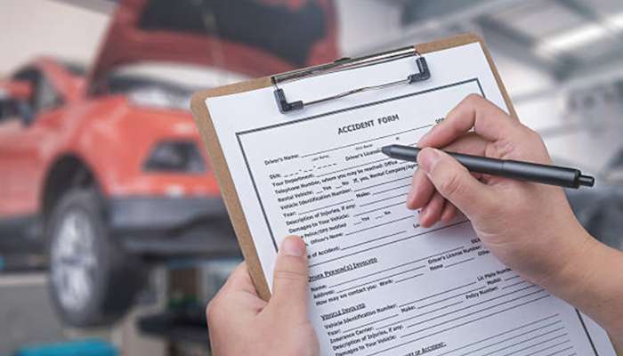 Person holding a clipboard with an accident form and pen in a repair shop, a red car in the background
