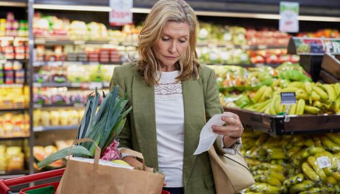 The 20-minute grocery bill reset 1 | tycoonstory media What are smart ways to save money on groceries? Shopper checking her grocery receipt while buying fresh vegetables at a supermarket.