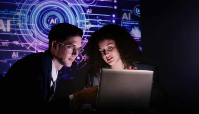 When ai meets cognitive assessment 1 | tycoonstory media Two professionals study a laptop together against a neon ai-themed backdrop in a dark room.