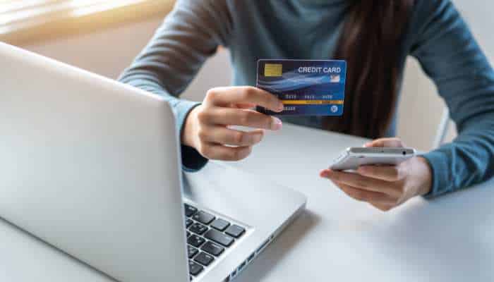 Cash back credit card user making an online purchase with laptop and smartphone for managing digital payments and rewards.
