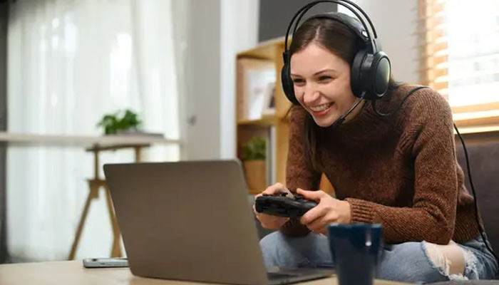 Woman wearing a gaming headset and holding a controller while enjoying xbox cloud gaming on a laptop from her living room.