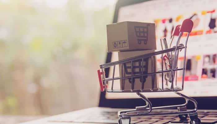 Miniature shopping cart with a cardboard box sits on a laptop keyboard, symbolizing online shopping.