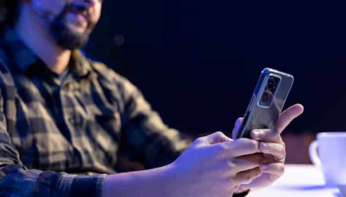 Man in a plaid shirt holding a smartphone at a table.