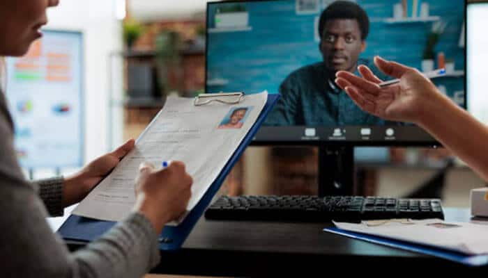 Speed to first hire depends on what's already in place | tycoonstory media Person taking notes on a clipboard while a teammate speaks on a video call shown on the monitor in front of them.