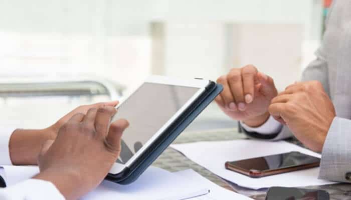 Moving from eor to your own entity takes preparation | tycoonstory media Two professionals use a tablet at a meeting, with smartphones on the table nearby.