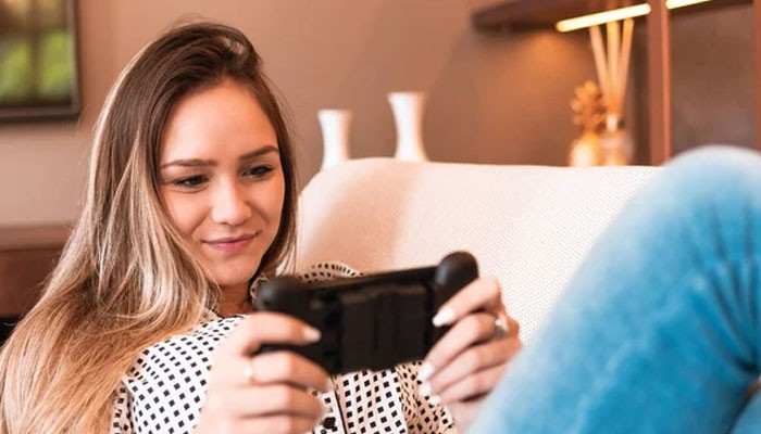 The role of mobile in live gaming growth | tycoonstory media Woman relaxing on a sofa, smiling, while playing a handheld game controller/phone.
