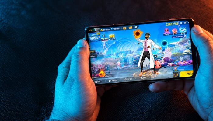 Unlock ff beta - tycoonstory | tycoonstory media Unlock ff beta illustration showing hands holding a smartphone displaying a free fire character lobby.