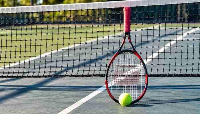 Why the mistake is so easy | tycoonstory media Tennis racket leaning against a net on an outdoor court with a bright tennis ball nearby