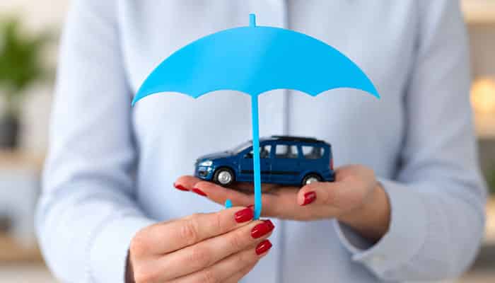 When umbrella insurance may not cover the claim | tycoonstory media Woman holding a blue umbrella over a toy car, illustrating how an umbrella insurance policy provides additional liability protection.